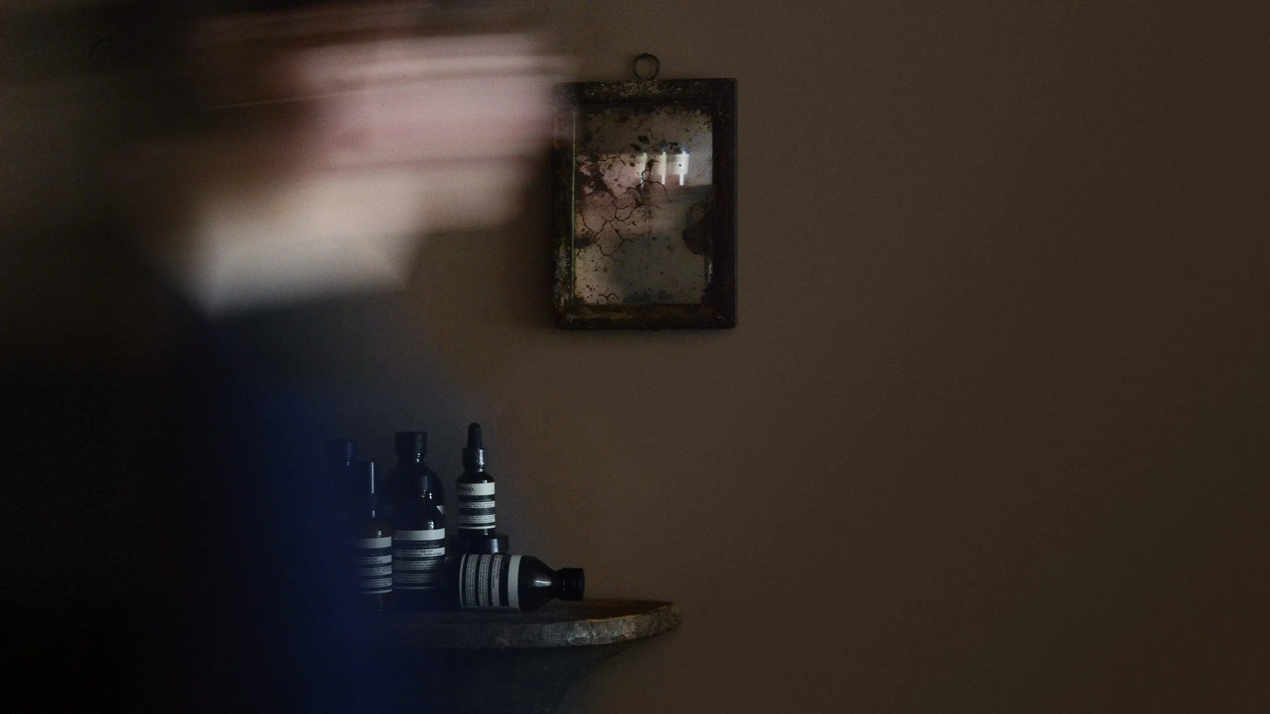 模糊的身影在老舊鏡子前移動，在背景中收集 Aesop 產品。