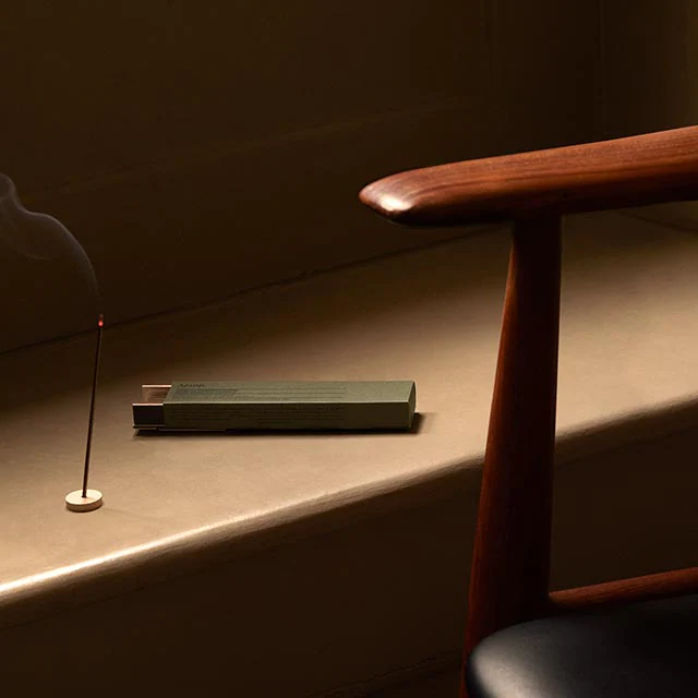 A lit stick of incense sitting alongside a mid-century chair.
