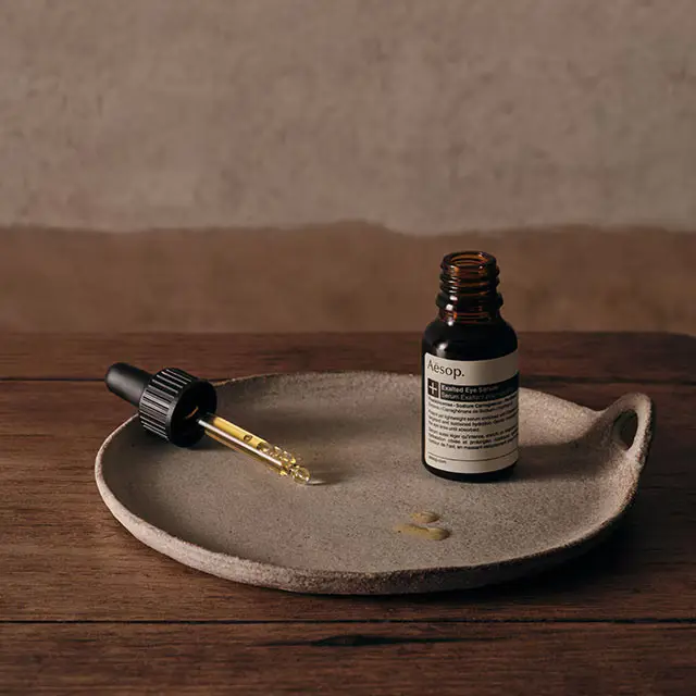 A ceramic plate and a bottle of exalted eye serum placed on a wooden surface