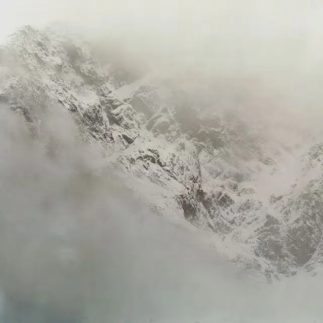 A winter snowy mountain surrounded by fog.