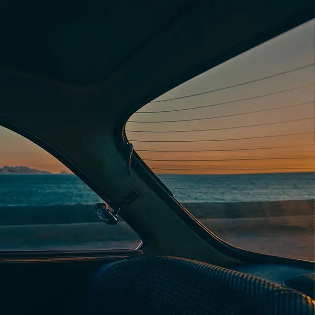 A car interior with a view of the ocean at sunset. 