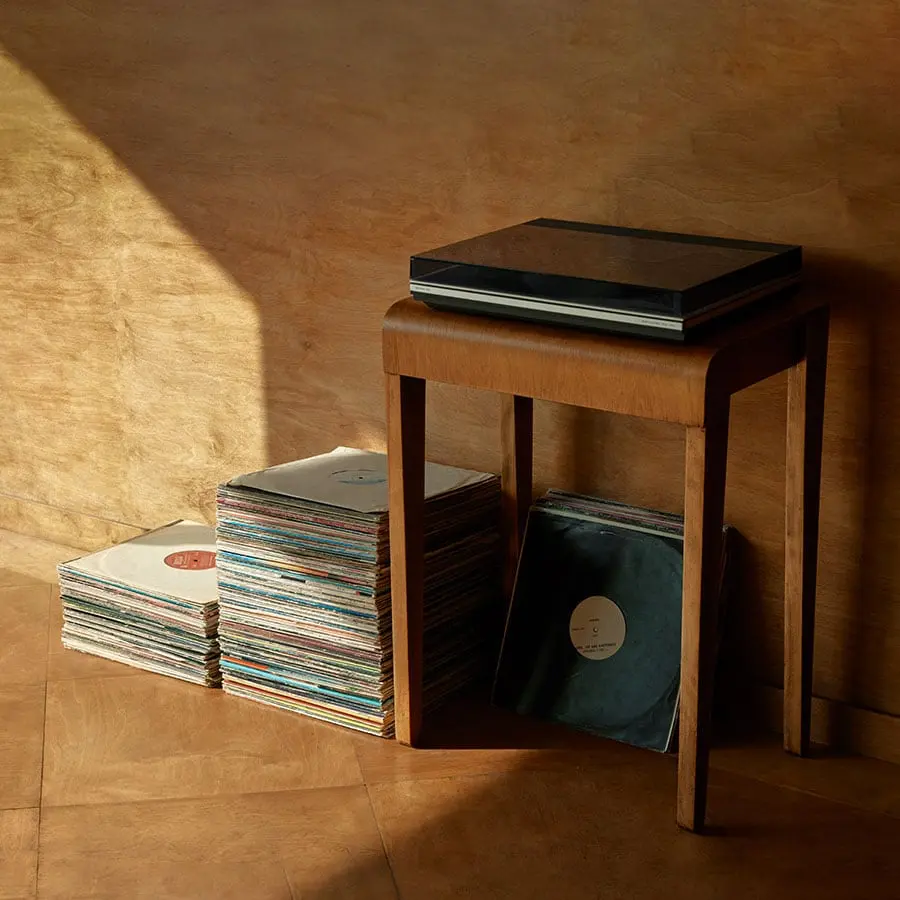 A turntable on a mid-century wooden table with a stack of vinyl records resting alongside it.